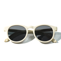 Oval sunglasses with light beige frame and dark lenses, front close view